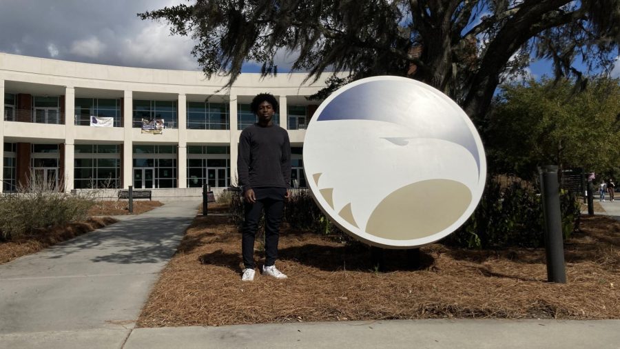 Rylan Artis posing next to the logo outside of the Student Union building.